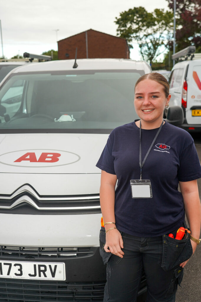 A portrait photo of a woman standing beside a branded 'AB' van, smiling at the camera.